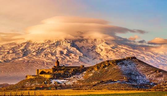 Snow-capped Mount Ararat with Khor Virap monastery on hillside at sunset in Armenia